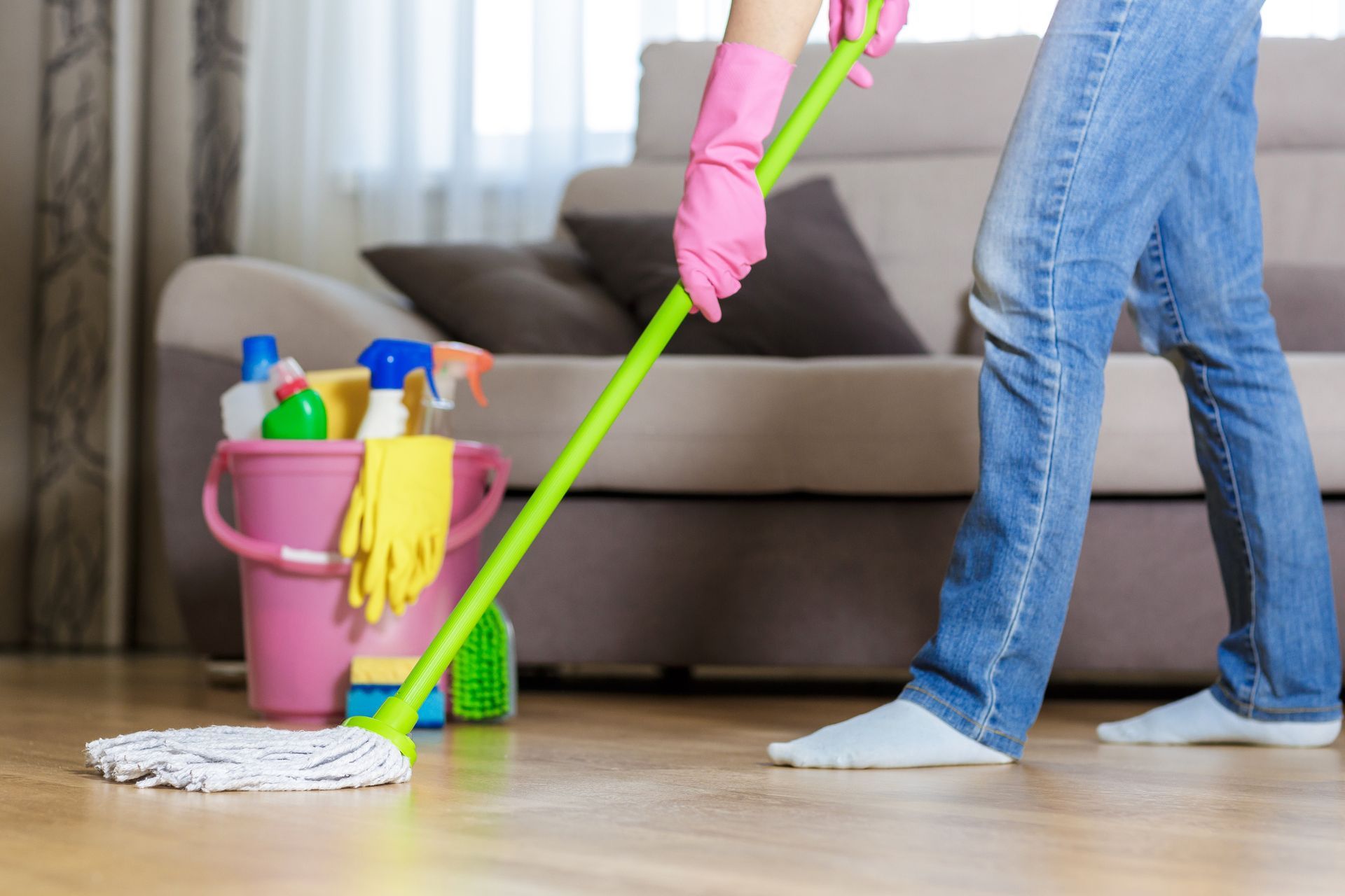 A woman in pink gloves is mopping the floor in a living room.