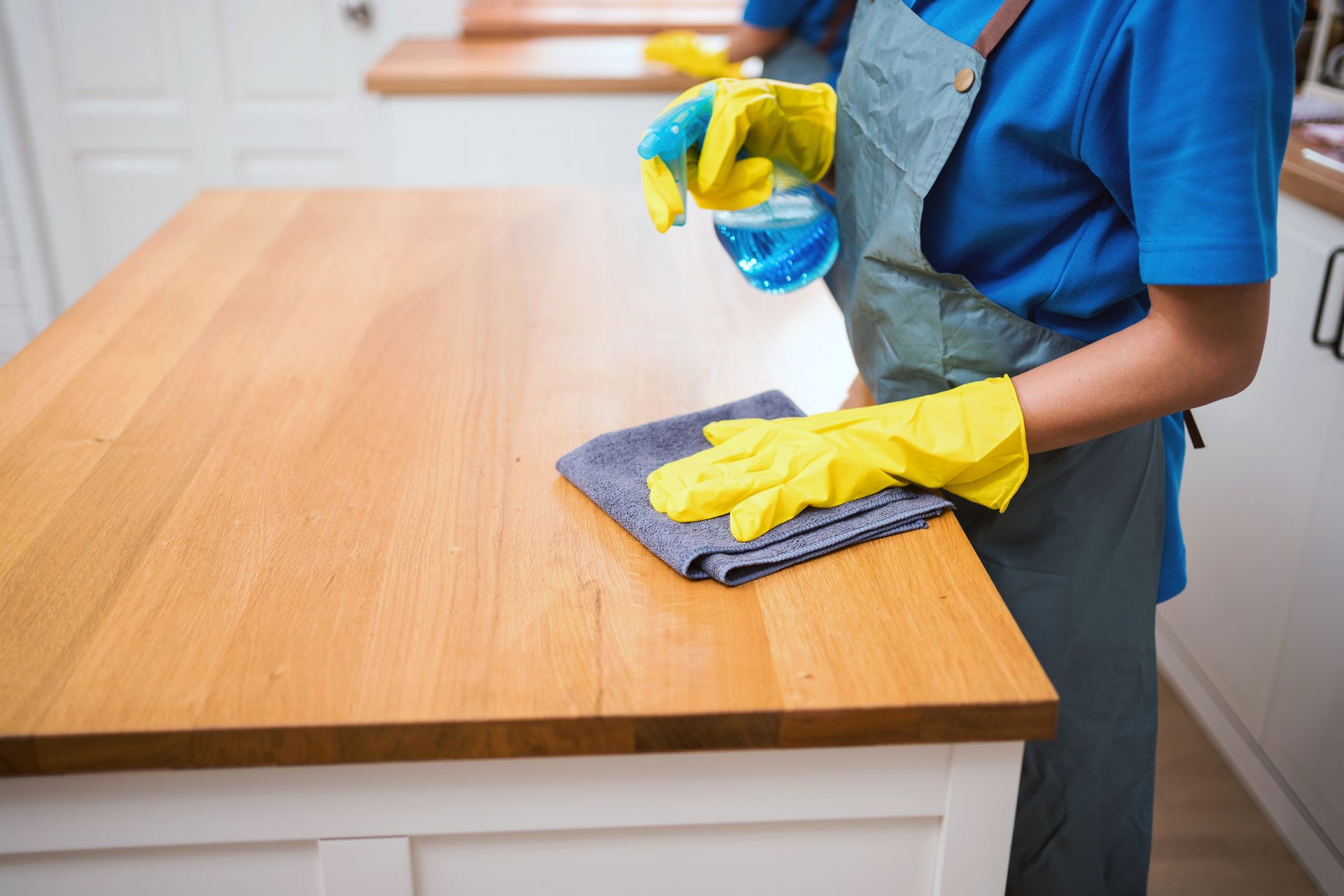 A woman wearing yellow gloves is cleaning a wooden counter in a kitchen.