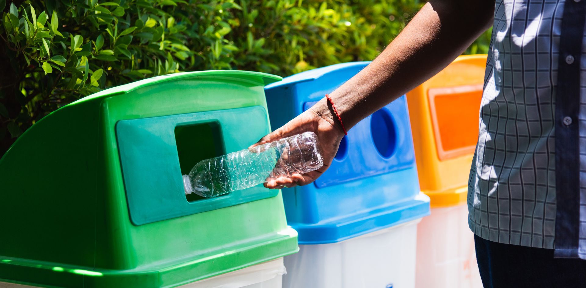 A person is throwing a plastic bottle into a recycling bin.