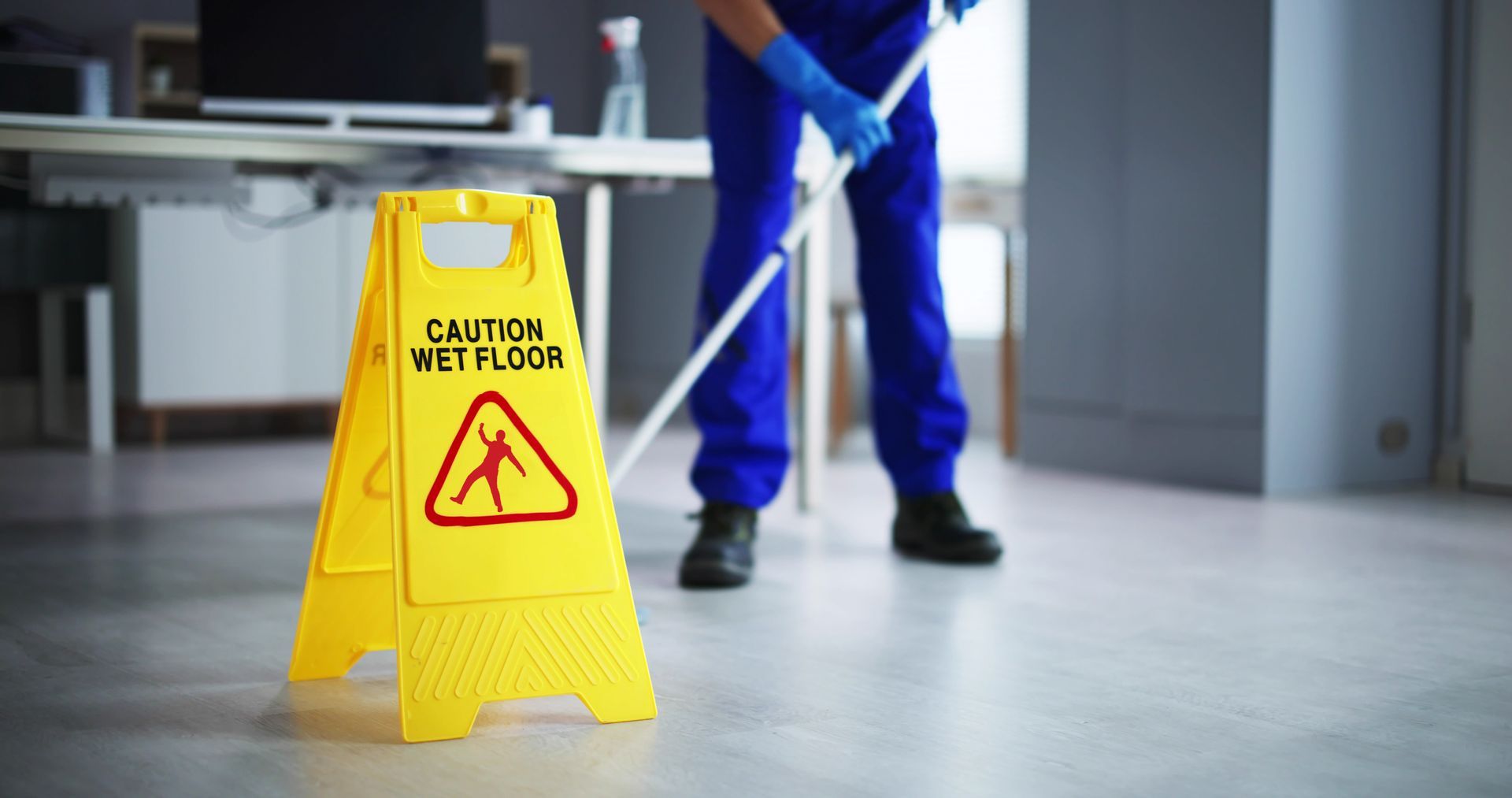 A man is mopping the floor next to a yellow caution-wet floor sign.