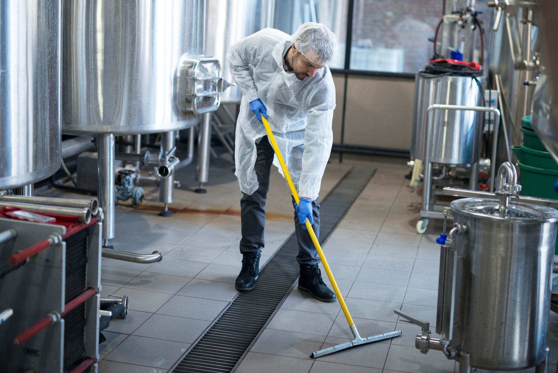 A man is cleaning the floor of a factory with a mop.